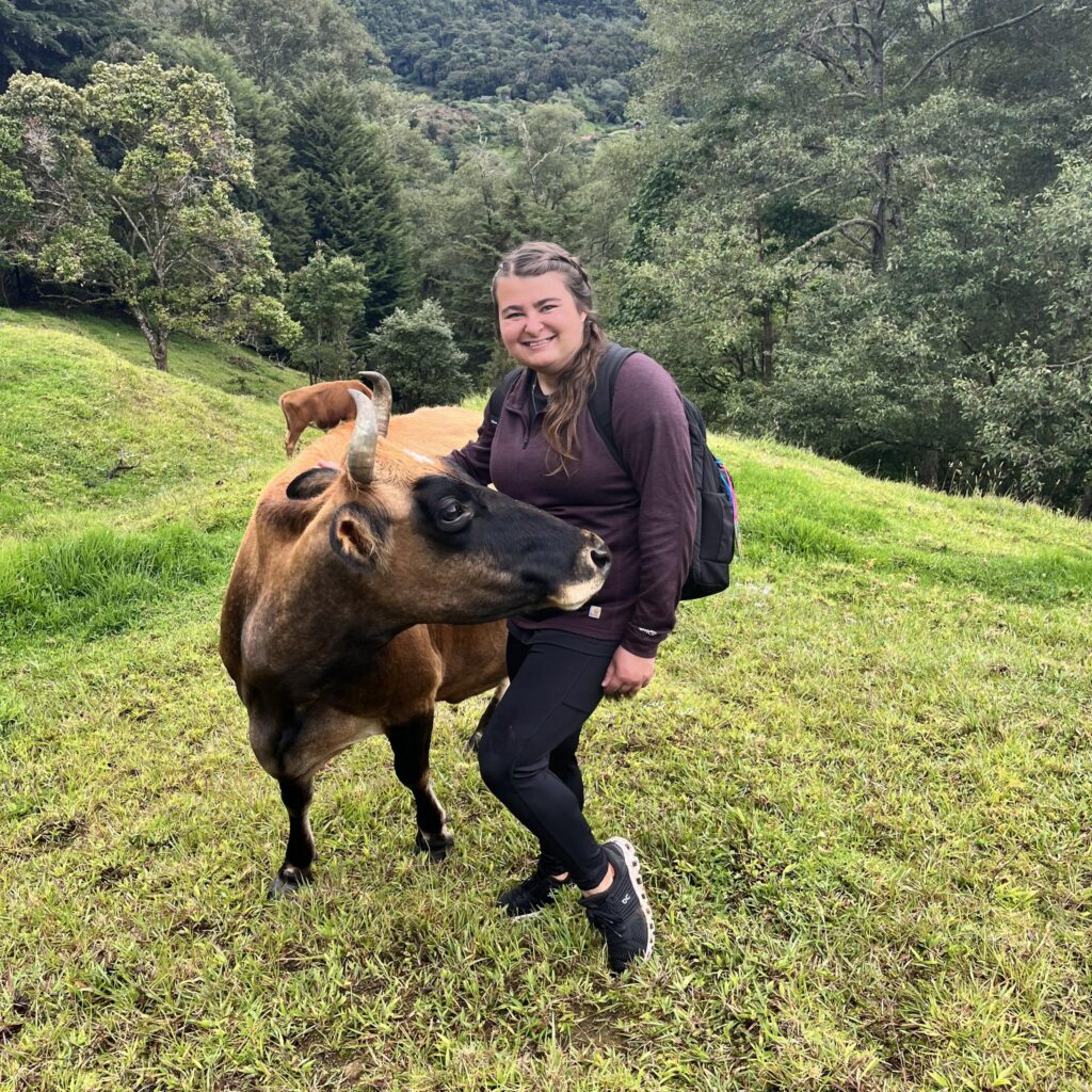 Abbie Joines poses with a cow on a hilly slope.